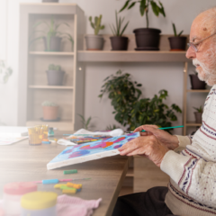 Elderly man with dementia painting at a table in a memory care setting, engaging in a therapeutic, creative activity.